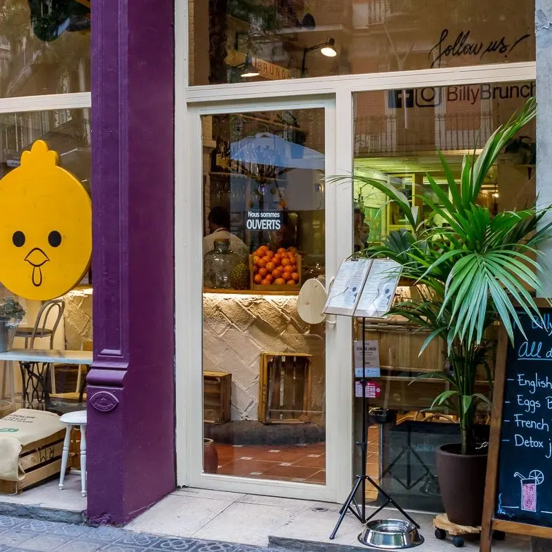 Fachada de Billy Brunch, acogedor café en Barcelona con cartel que anuncia desayunos todo el día como Eggs Benedict, French Toast y jugos detox.