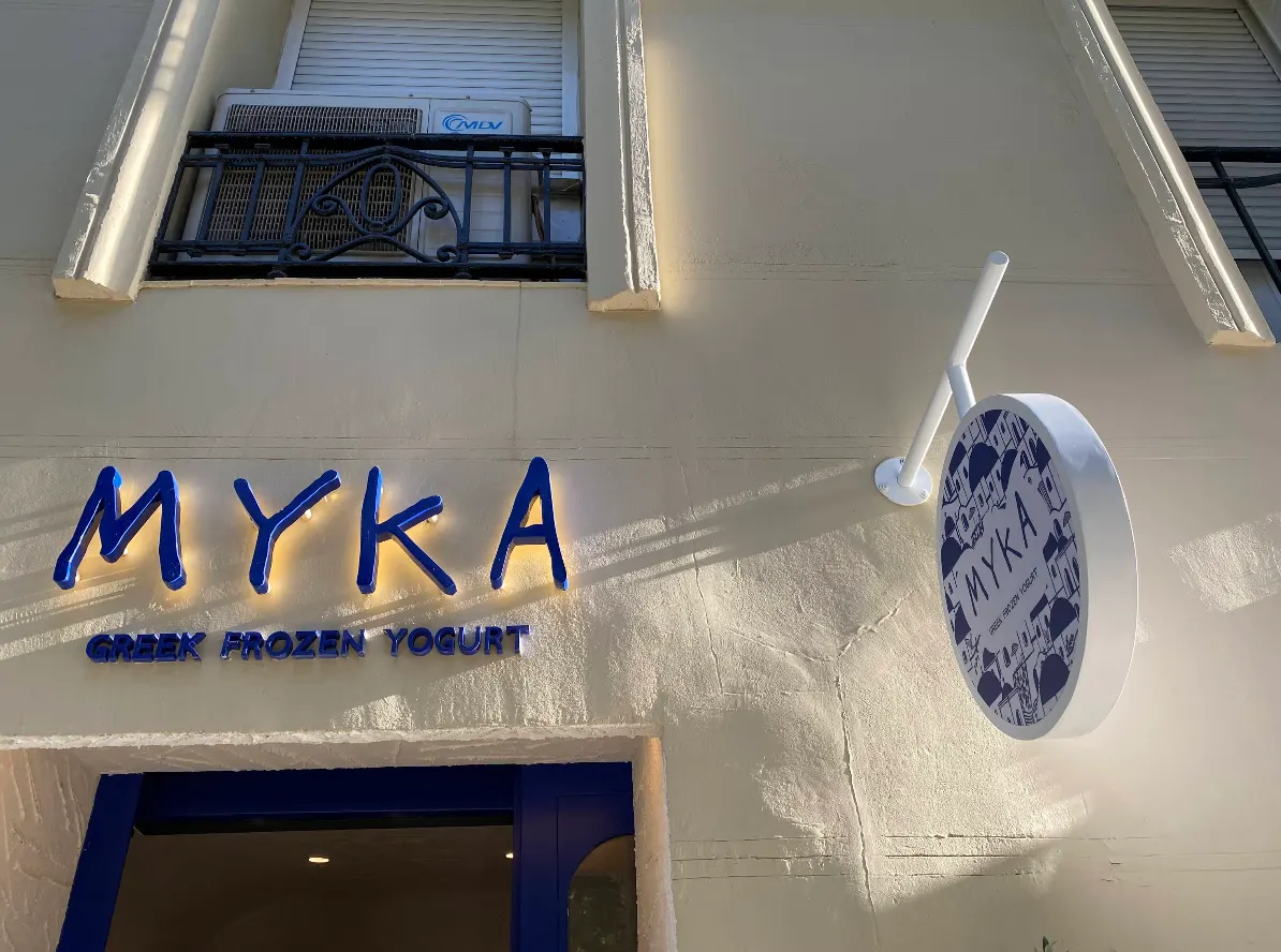 Fachada de Myka Ortega y Gasset con letras azules retroiluminadas y rótulo circular decorado con motivos griegos.