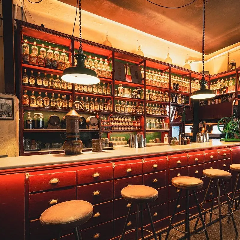 Barra vintage en Dr. Stravinsky, con taburetes altos, botellas organizadas en estanterías y una decoración cálida que evoca un laboratorio antiguo.