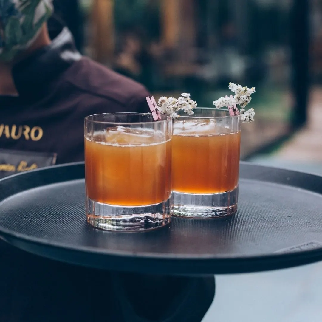 Elegantes cócteles servidos en vasos cortos, adornados con un toque floral, destacando una mezcla balanceada y sofisticada. La presentación es ideal para una experiencia de degustación refinada en un ambiente exclusiv