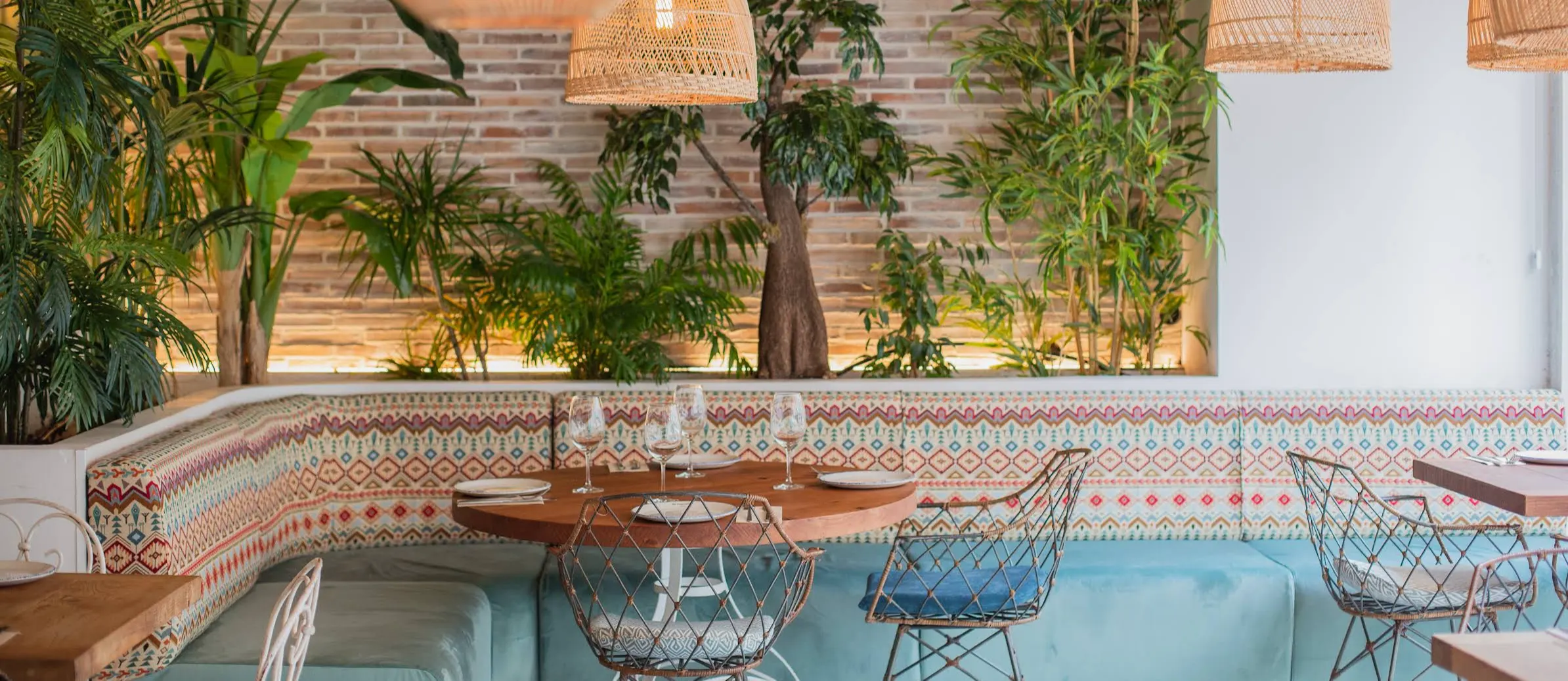 La imagen muestra un espacio interior, de La Mamona con un ambiente acogedor e invitador. El entorno incluye varias mesas con sillas y asientos tipo banco a lo largo de una pared. La pared está decorada con azulejos decorativos.
