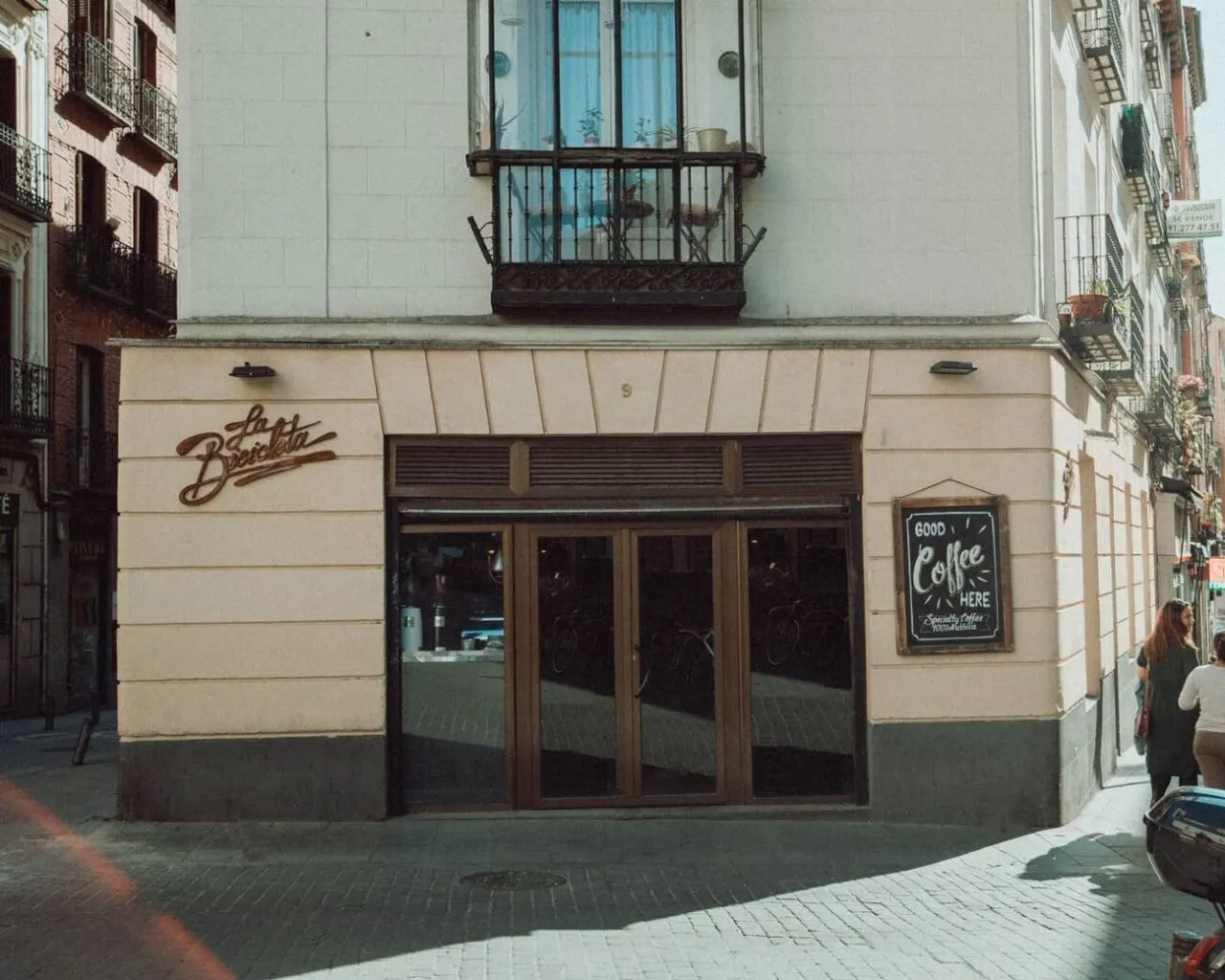Fachada del café La Bicicleta en una esquina de Malasaña, con cartel de “Good coffee here” y puerta de entrada acristalada.