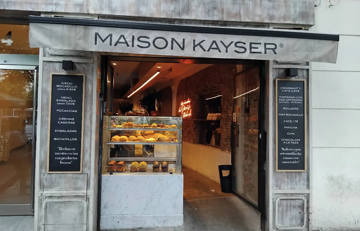 Maison Kayser Quevedo muestra su fachada de piedra clara con un toldo gris y una vitrina llena de bollería artesanal.