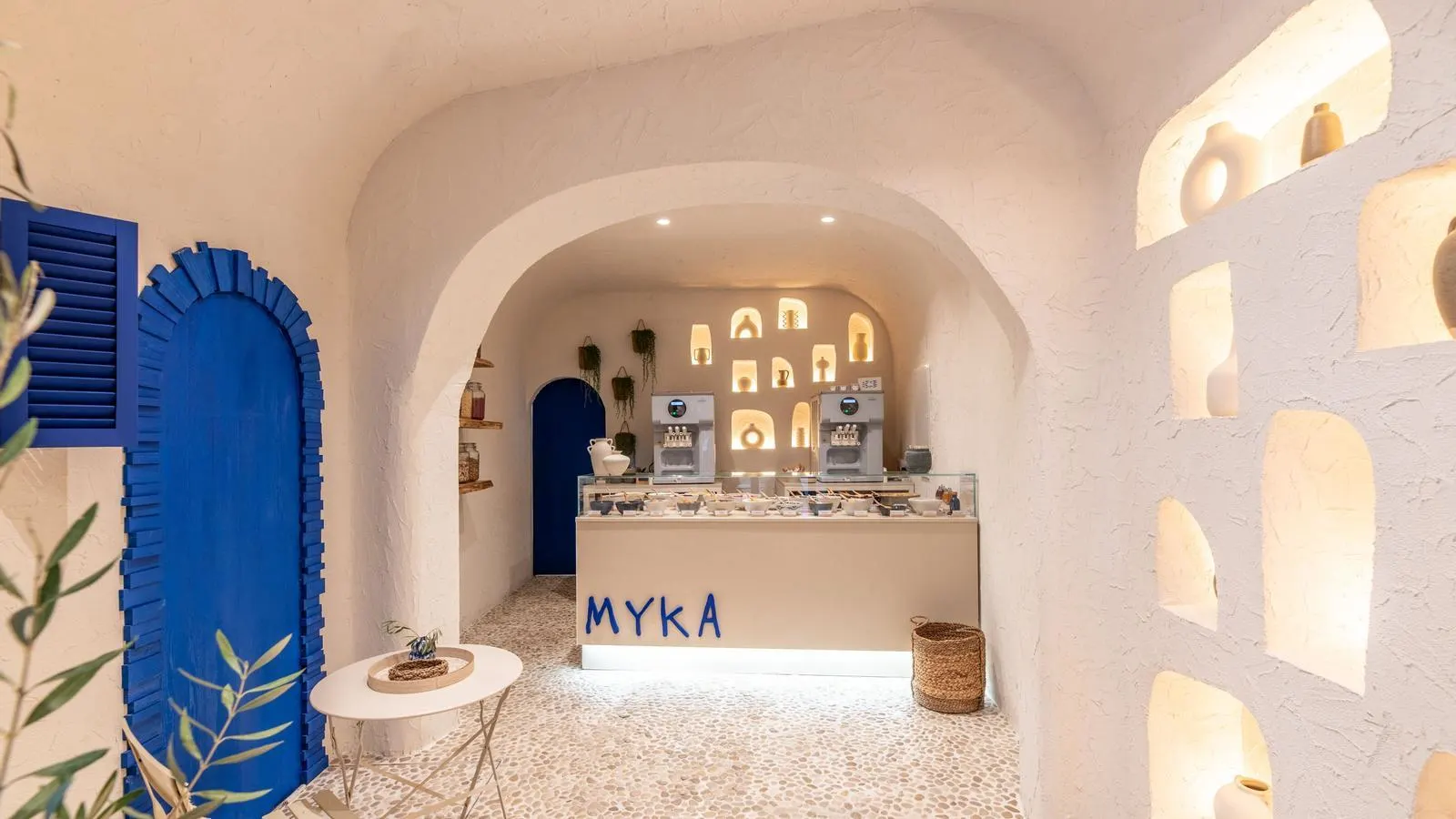 Interior de Myka Ponzano con estética mediterránea, paredes blancas, detalles en azul intenso y vitrinas de helado bajo arcos iluminados.