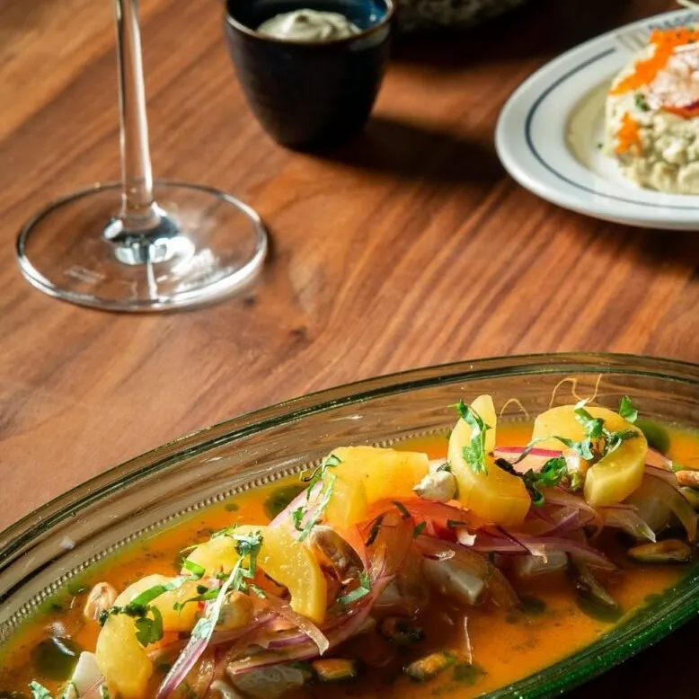 Mesa con vino blanco, marisco con hierbas y fruta, panecillos, salsa y ensalada cremosa con huevas naranjas.