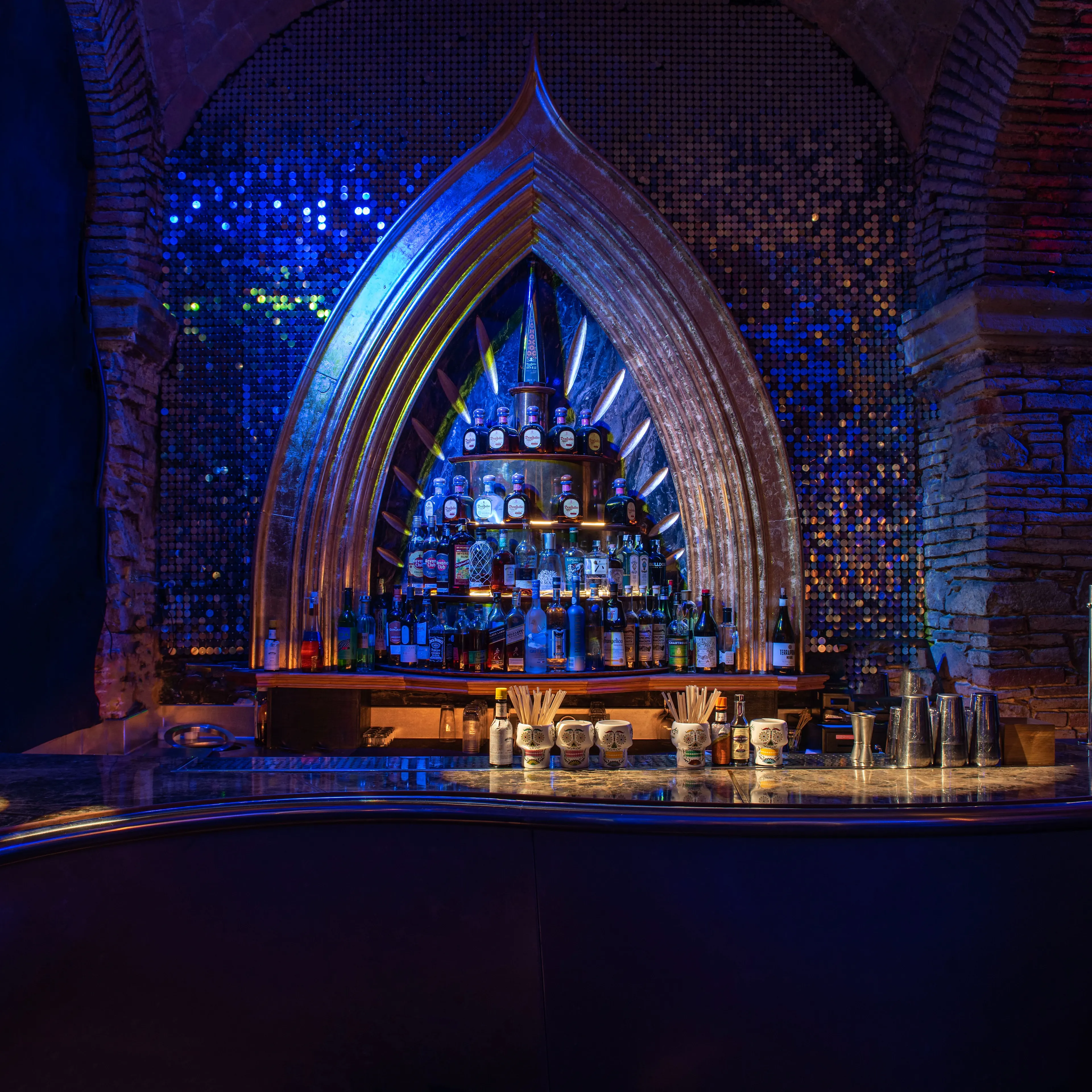 Monk deslumbra con su barra central rodeada de una estructura dorada y paredes de mosaicos azules, creando un espacio elegante y moderno.