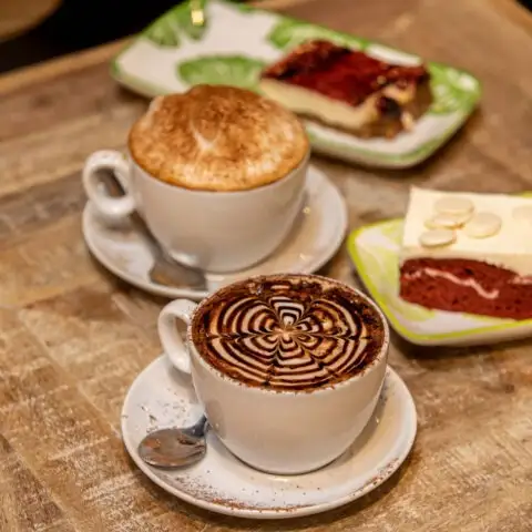 Cafés decorados y tartas irresistibles sobre mesa rústica en Julieta Coffee. El plan perfecto para una pausa dulce y reconfortante.