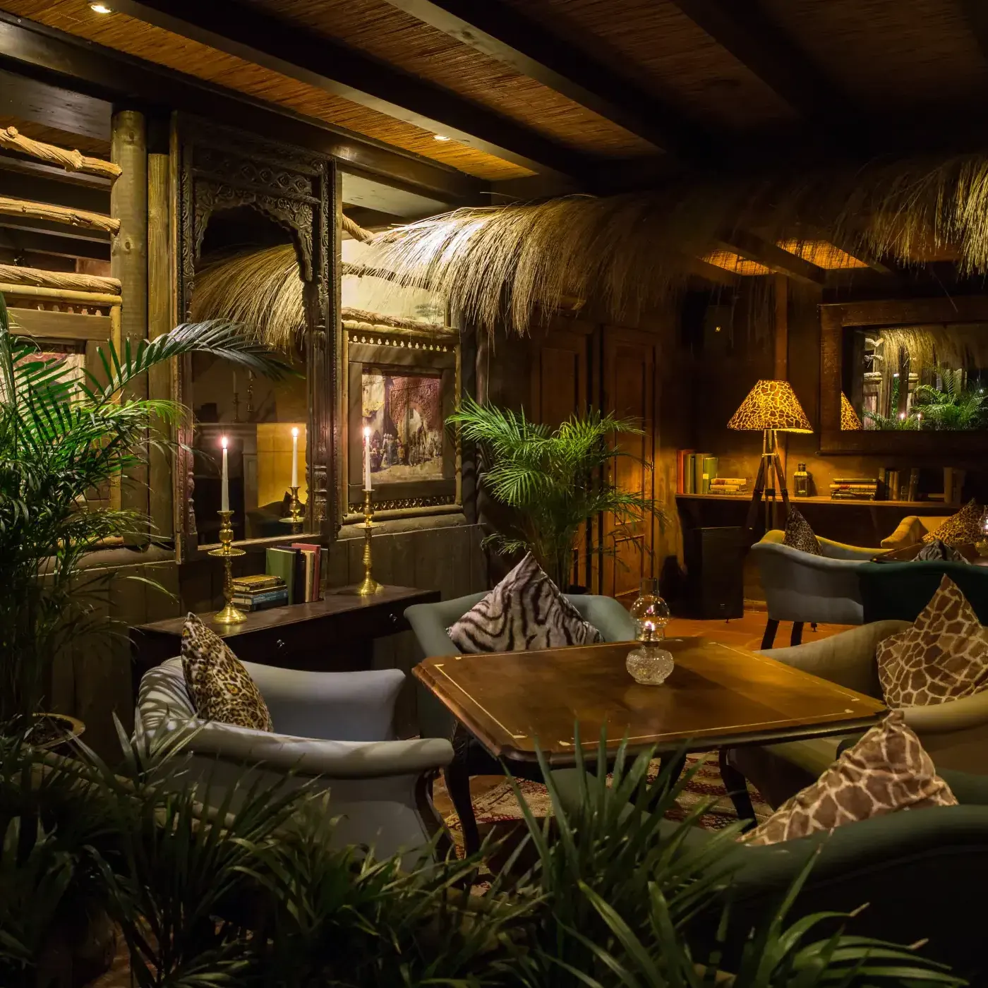 Ambiente cálido y exótico de Trocadero Sotogrande, con sofás elegantes, iluminación tenue, detalles de inspiración africana y abundante vegetación.