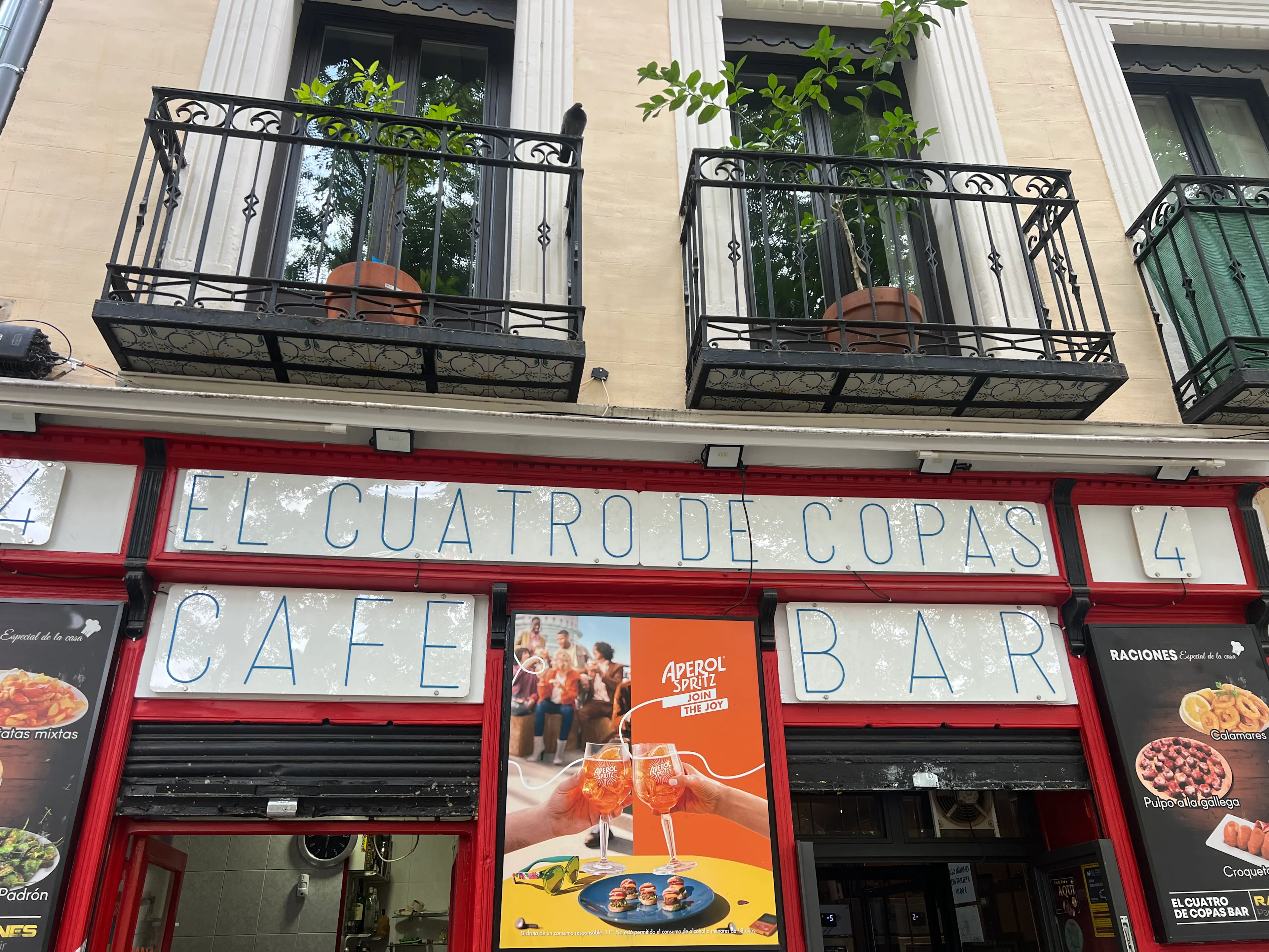 La fachada del bar El Cuatro de Copas muestra su cartel en letras azules con marcos rojos y balcones con macetas sobre la entrada.