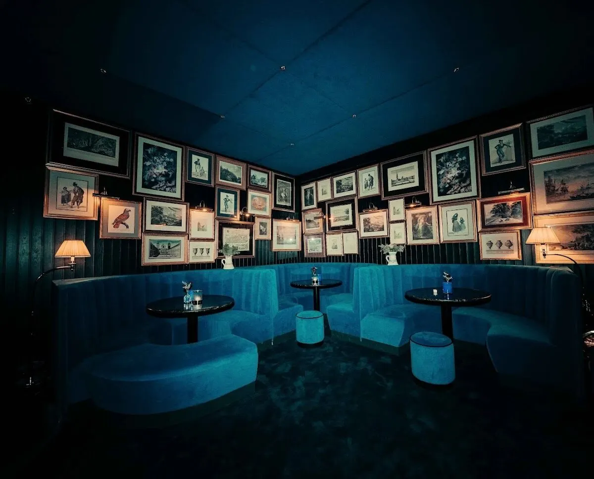 Intimate seating at La Estrella with velvet blue banquettes, framed vintage art covering the walls and warm ambient lighting from classic lamps.