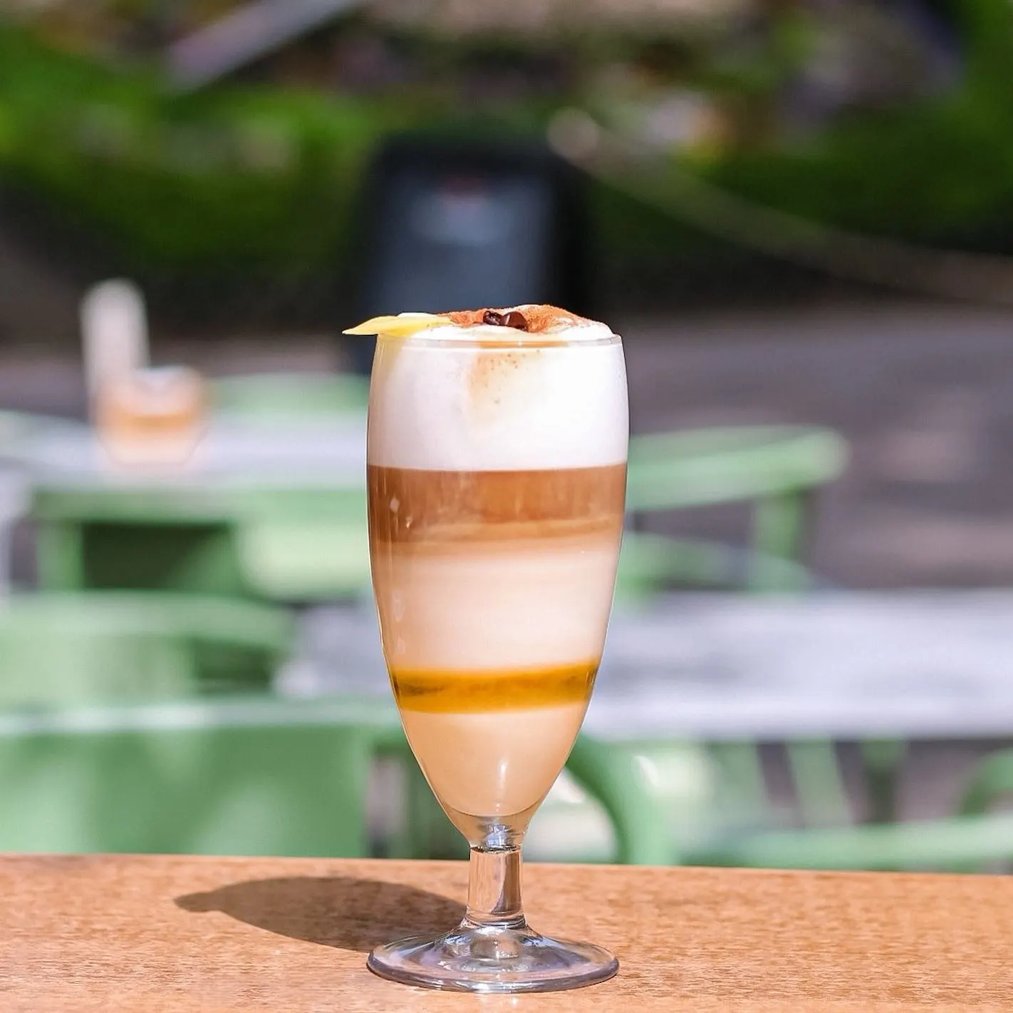 Cóctel en Terraza Parque con capas de crema y café, decorado con piña y granos de café. Ambiente soleado y relajado al aire libre.