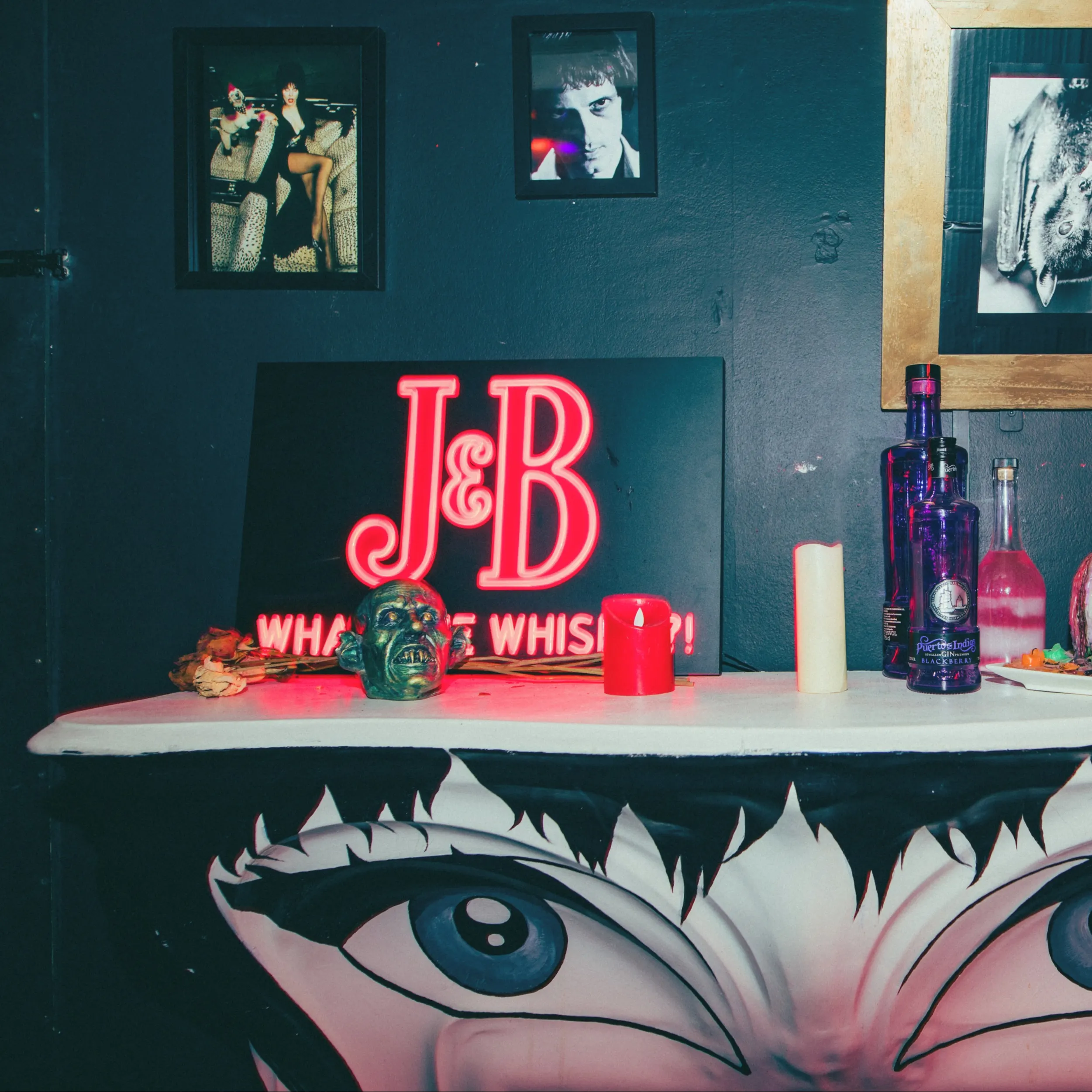 " Mesa decorada con temática oscura, luces de neón, botellas y detalles siniestros, creando una atmósfera intrigante y teatral."