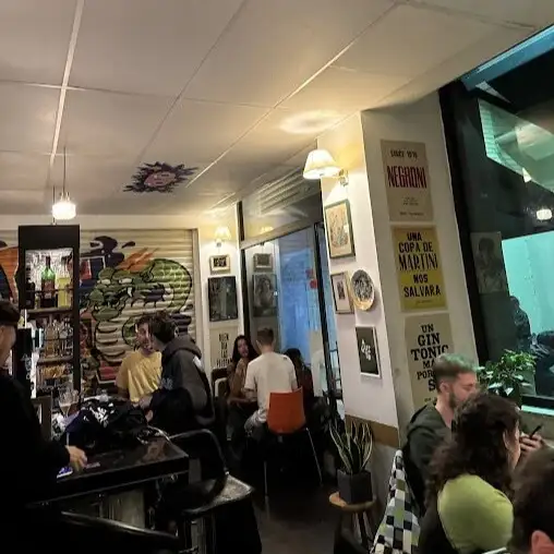 Café con barra, clientes conversando, póster de Negroni en la pared, luces colgantes y ambiente relajado.