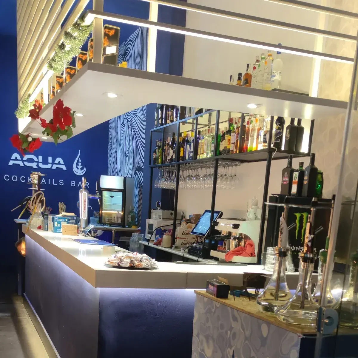 AQUA Cocktails Bar destaca por su diseño moderno, barra iluminada y amplia selección de bebidas, creando un ambiente vibrante y acogedor.