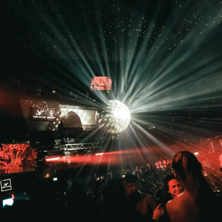 Escena de discoteca con bola de espejos, luces estrelladas en el techo, pantallas con visuales y ambiente oscuro con efectos de color.