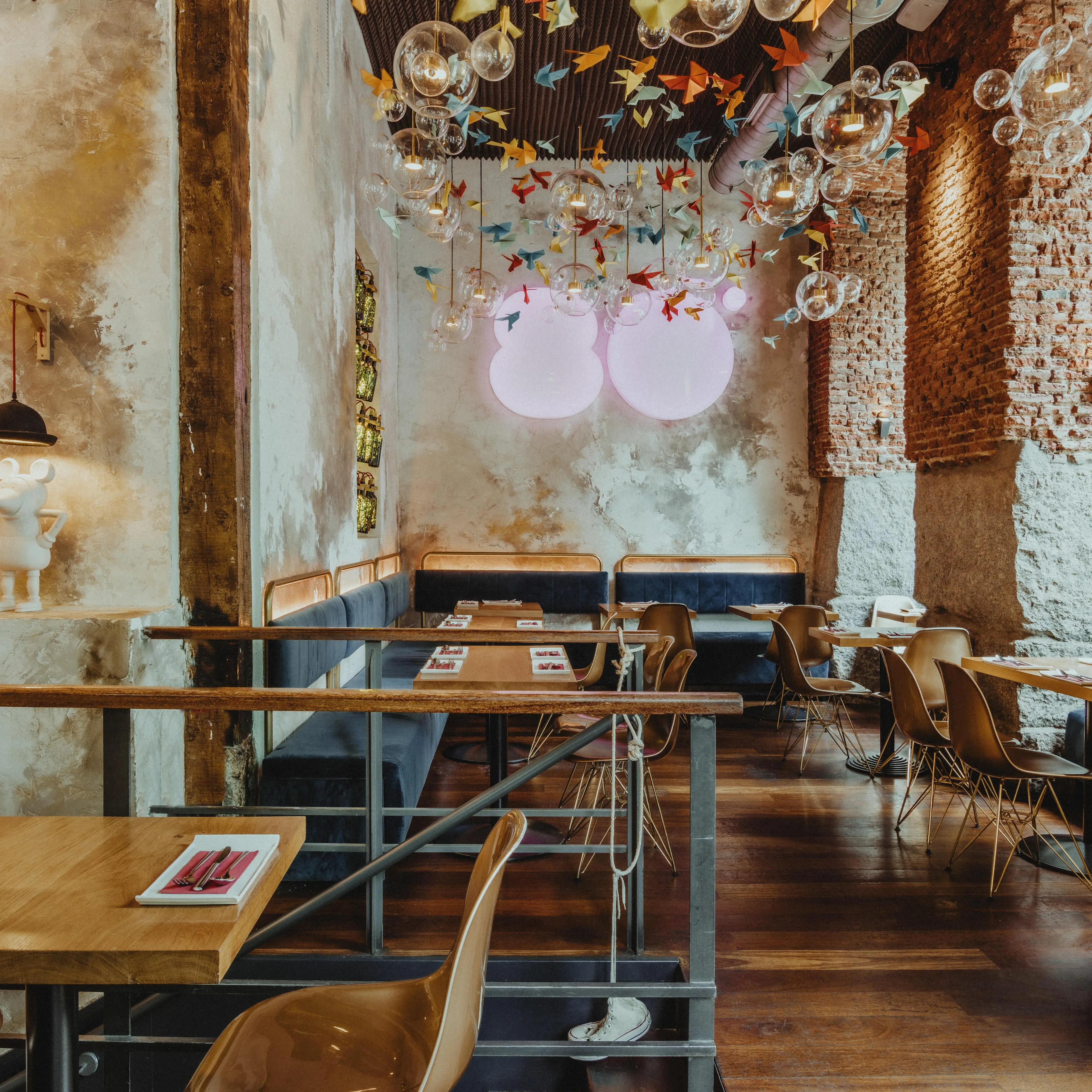 Interior de Ochenta Grados Malasaña con muros de ladrillo visto, lámparas de burbujas, grullas de papel y mesas de madera con estilo industrial y artístico.