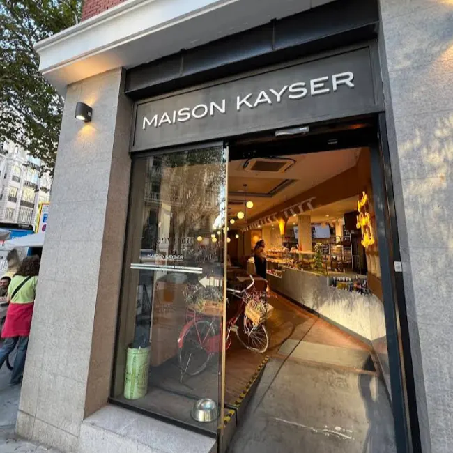 Entrada de Maison Kayser en Príncipe de Vergara, con fachada elegante, bicicleta decorativa y vistas al interior lleno de productos artesanos.