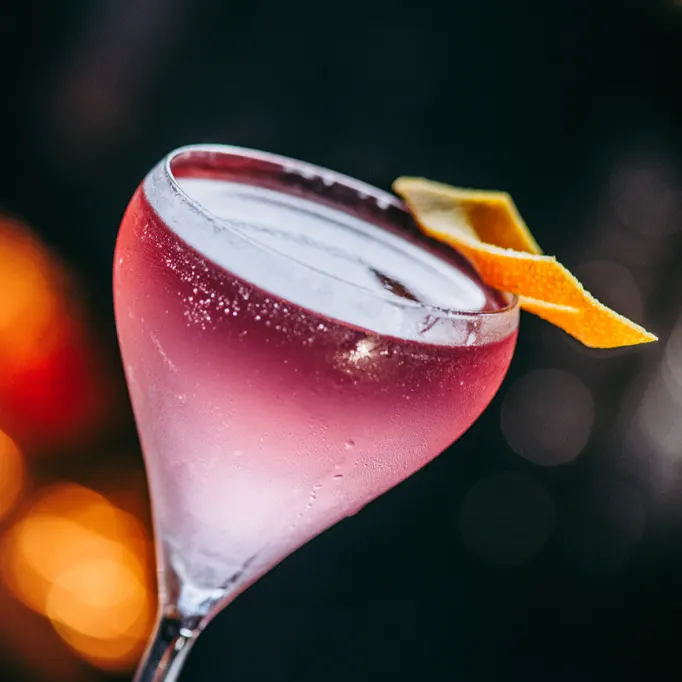 Un cóctel refrescante y vibrante en Mudanzas, con tonos rosados y un delicado twist de cítricos, perfecto para una noche especial.