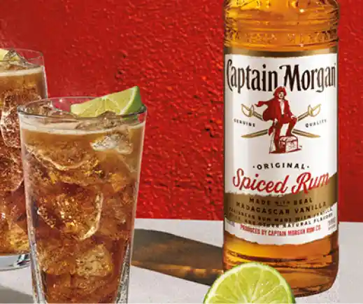 Botella Captain Morgan y vaso de longdrink con refresco de cola, ron y lima sobre mesa