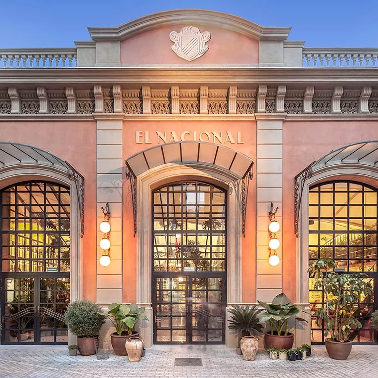 La fachada majestuosa de El Nacional, en tonos cálidos, grandes ventanales y rodeada de plantas que invitan a descubrir su interior.