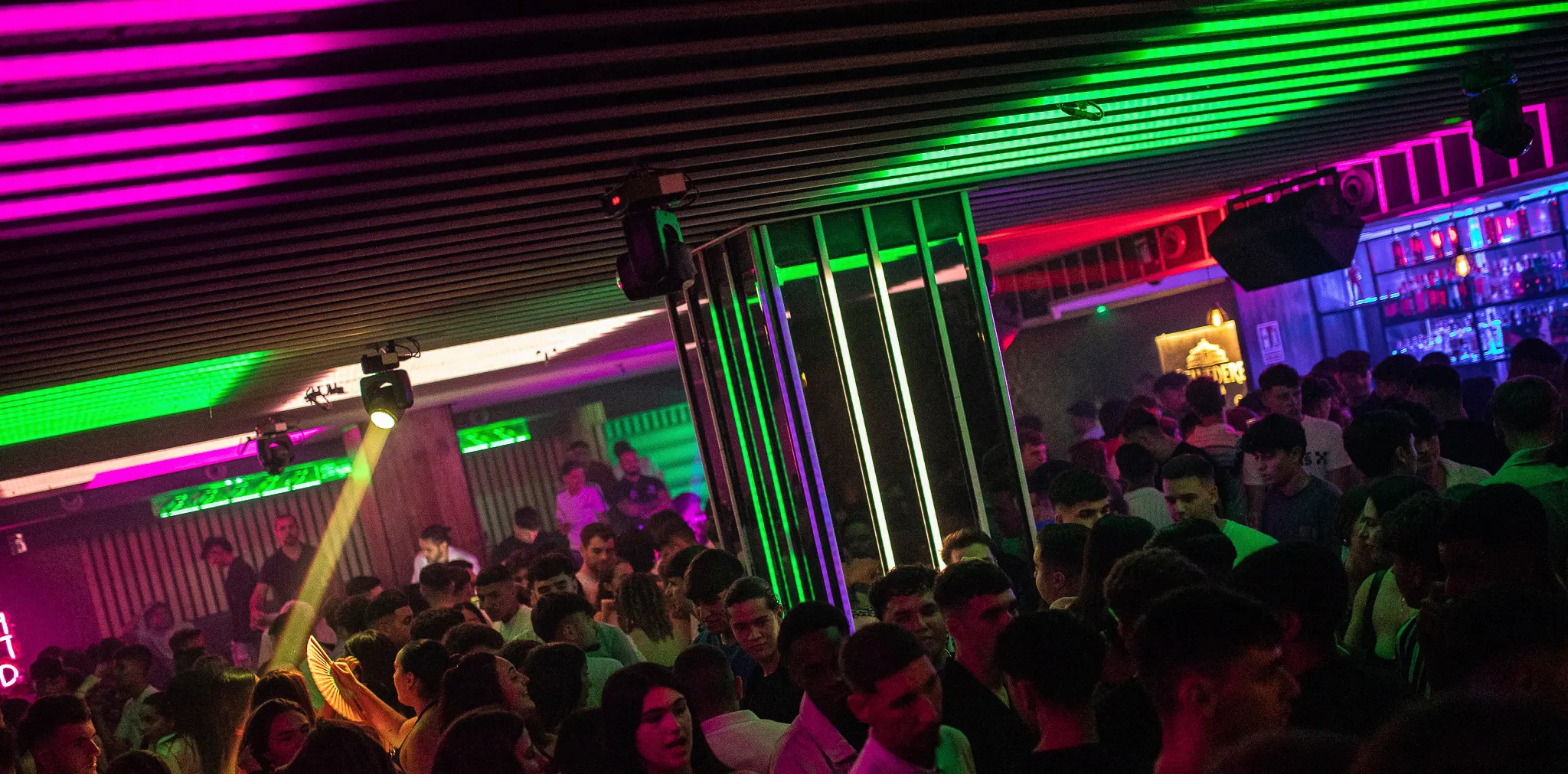 Pista de baile llena en Coltan y Benavente con luces verdes y púrpuras. Ambiente vibrante y multitud disfrutando de la noche.