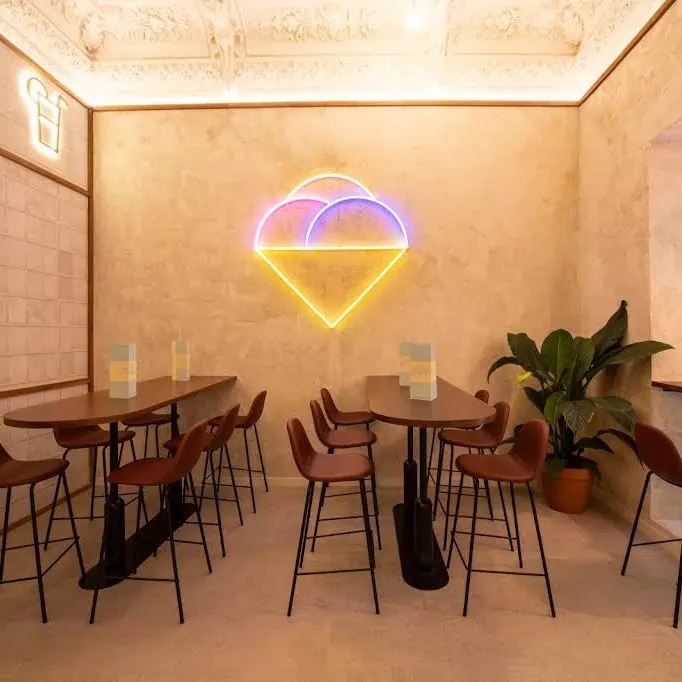 Sala de Mistura Plaza del Ángel con neón en forma de helado, mesas altas, sillas de diseño y plantas que aportan frescura.