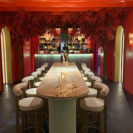 Espacio interior del karaoke con un ambiente moderno y acogedor. Hay un gran sofá esquinero azul bajo un espejo circular en la pared. Delante del sofá hay dos mesas de centro redondas con velas. A la izquierda, hay un mueble oscuro con fotos enmarcadas.