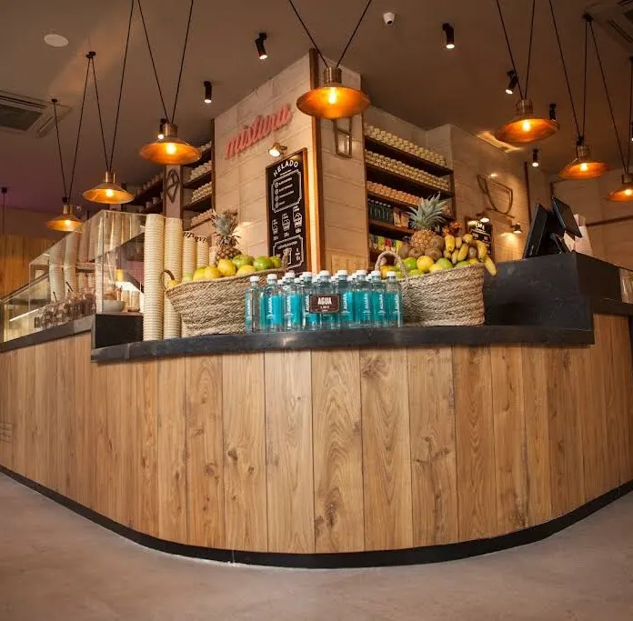 Mostrador interior de Mistura calle de Toledo con fruta fresca, conos apilados, botellas de agua y una estética cálida de madera y luz ámbar.