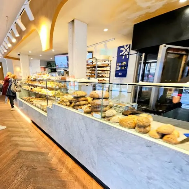 Vitrina de panadería en Maison Kayser Príncipe de Vergara, repleta de panes artesanos sobre mostrador de mármol en un local amplio y luminoso.