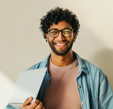 Smiling man with glasses holding an open laptop.