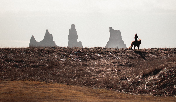 Silhouetted rider on horseback against a rugged Icelandic landscape with rock formations near Reykjavík in the background.