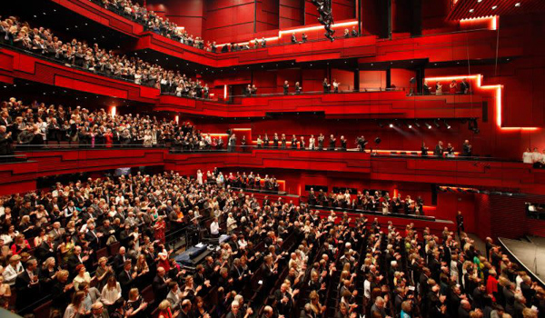 Crowded Harpa Reykjavík auditorium filled with audience during an event, red seats and balconies visible.
.
