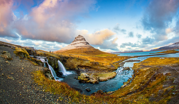 Scenic view of Kirkjufell mountain with cascading waterfall, vibrant autumn landscape, and a flowing river in Iceland.