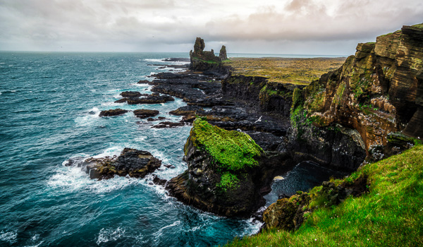 Dramatic cliffs and rugged coastline at Djúpalónssandur beach with crashing waves and lush green vegetation