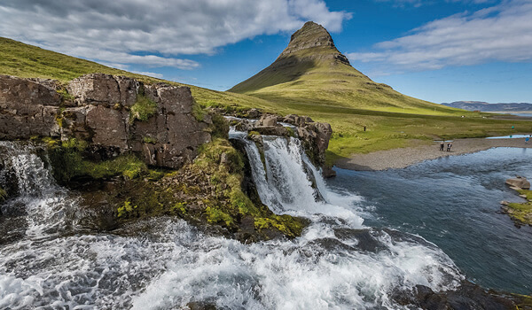 Scenic view of Kirkjufellsfoss waterfall with the iconic Kirkjufell mountain in the background under a partly cloudy sky in Iceland.