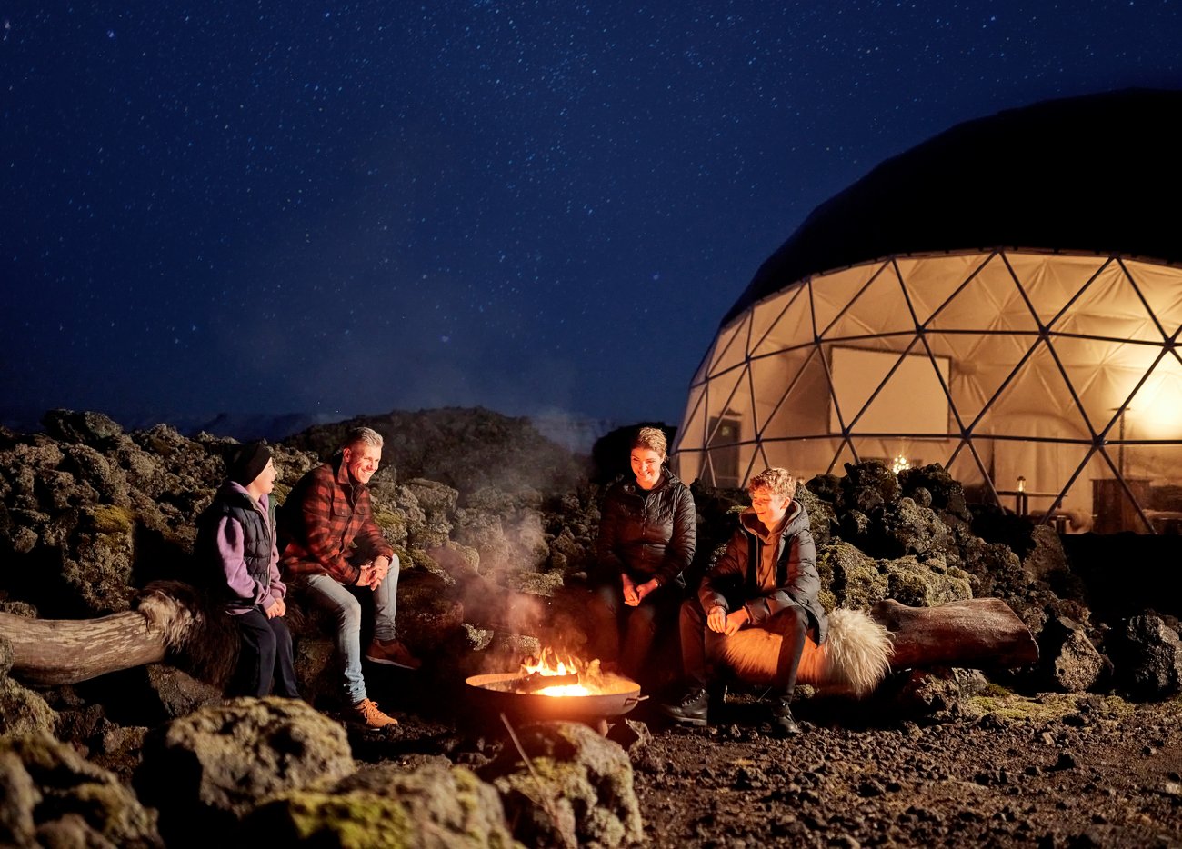 family sitting in front of Aurora basecamp at campfire