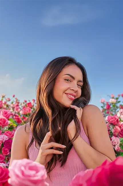 Mujer entre rosas con el cabello suelto. Texto: “Pelo más suave, con movimiento natural y perfume duradero”