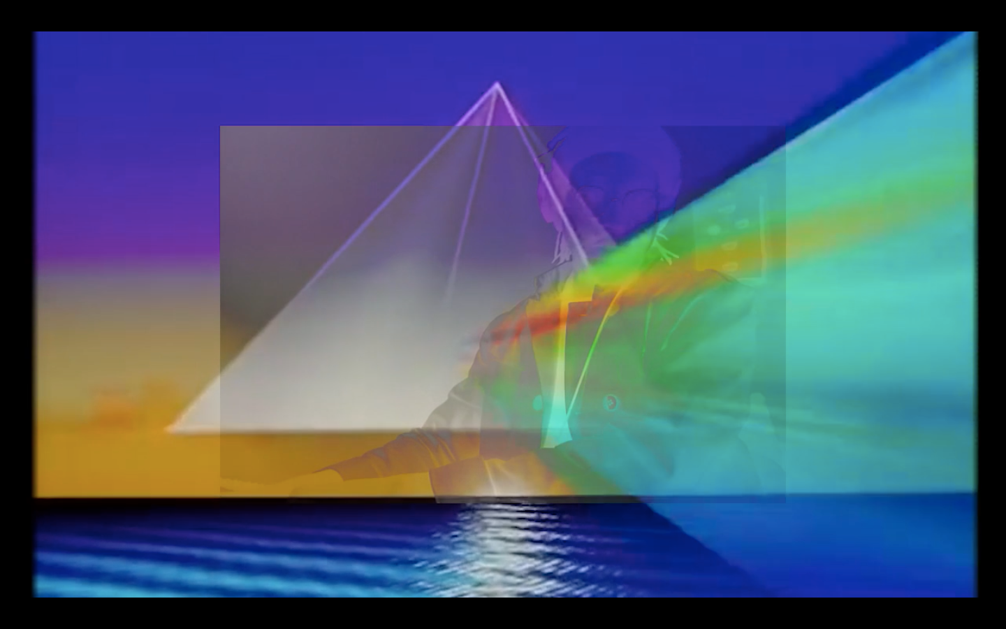 A video still showing a digital rendering of a ocean, horizon line, and sky. A gray pyramid shape floats over this with a rainbow prism emerging from its center. Below that, a negative image of the artist can be seen.