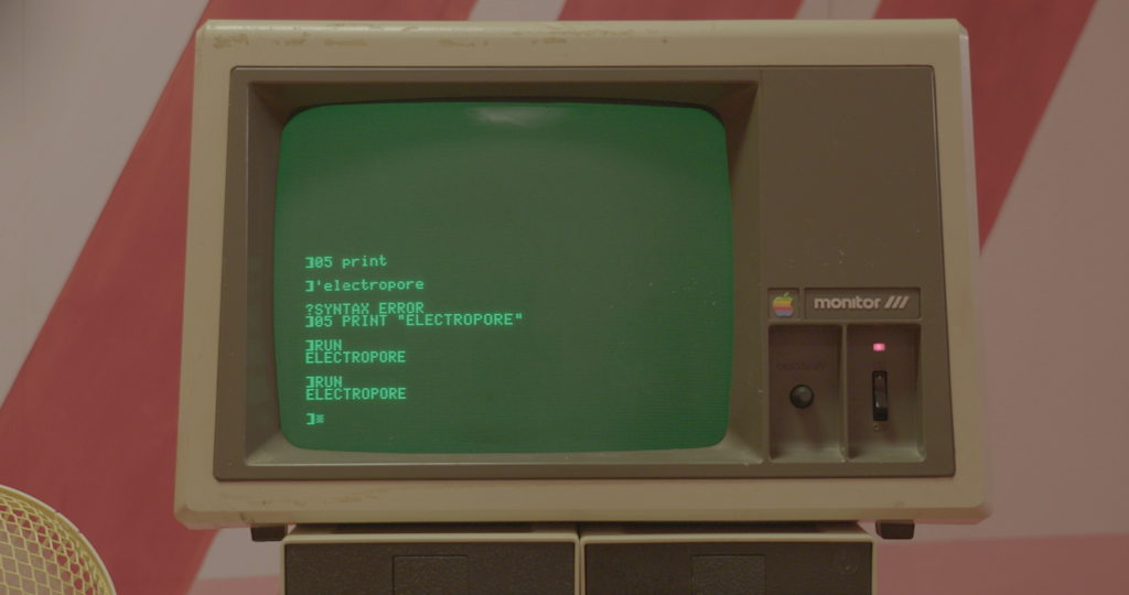 An early generation Apple computer monitor is show. There is code visible on the screen.