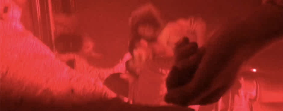 A blurry image shows several people standing close together bathed in red light. 
