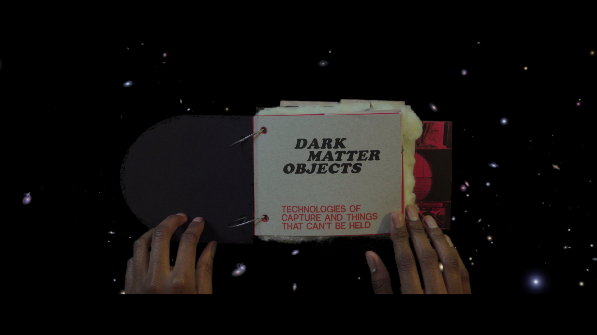 Two hands hold open a handmade book that has cotton forming a border around an archival B&W image of people working in the cotton fields. In the background, the same archival image is shown.