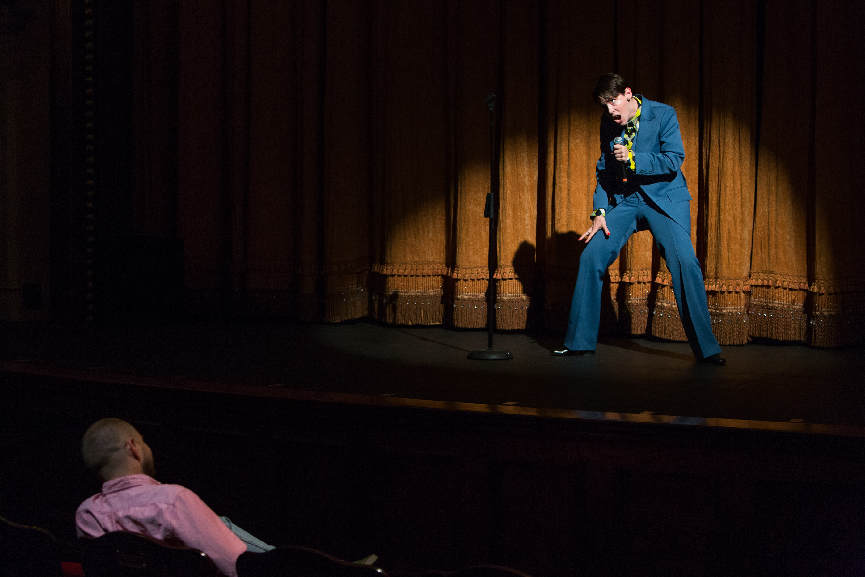 Sophia is standing on stage with mic in front of gold curtain