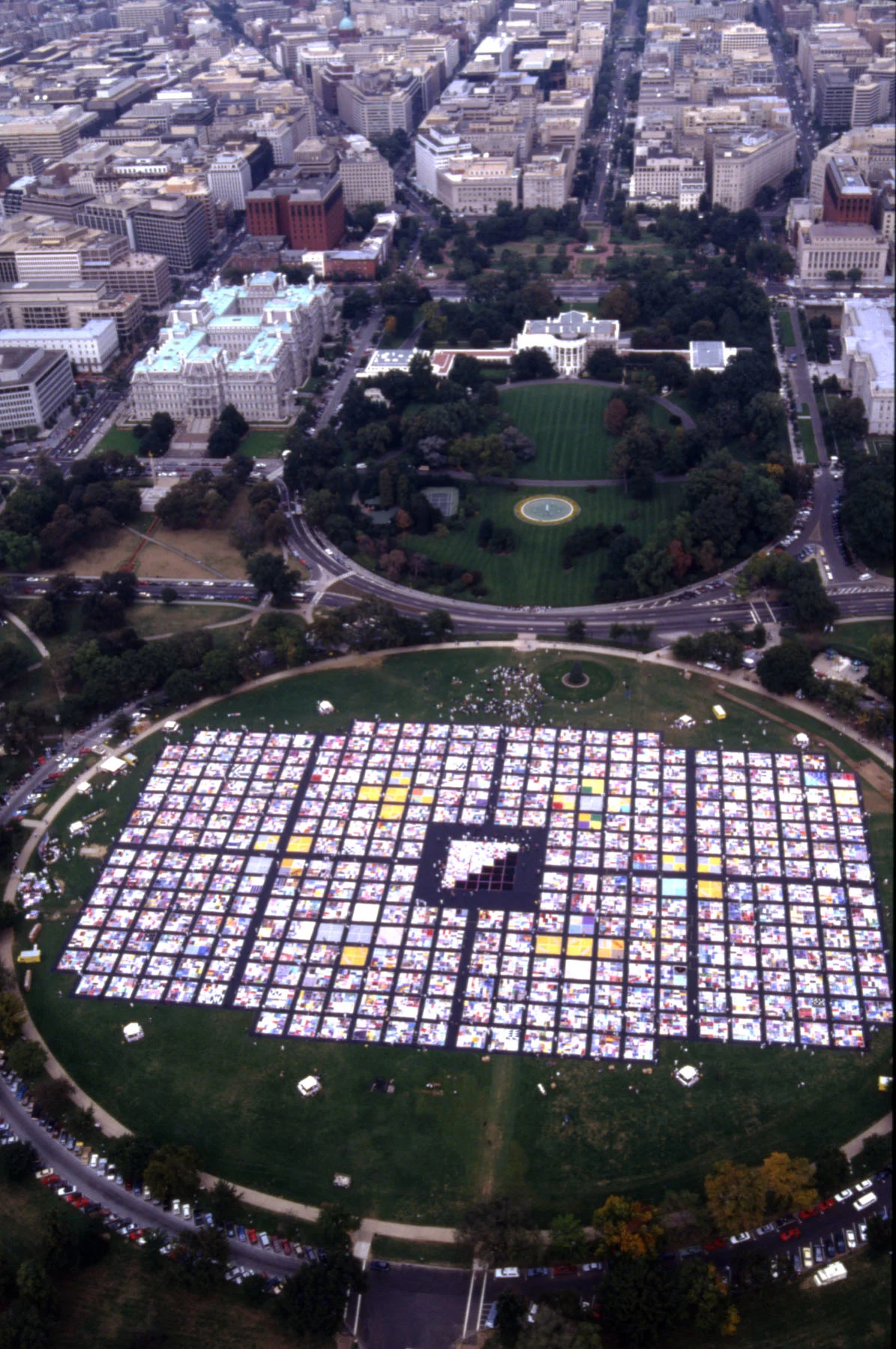 A color photograph showing a bird’s eye view of the White House and the lawn in front of it, covered in hundreds of quilts, laid out next to each other in neat rows.