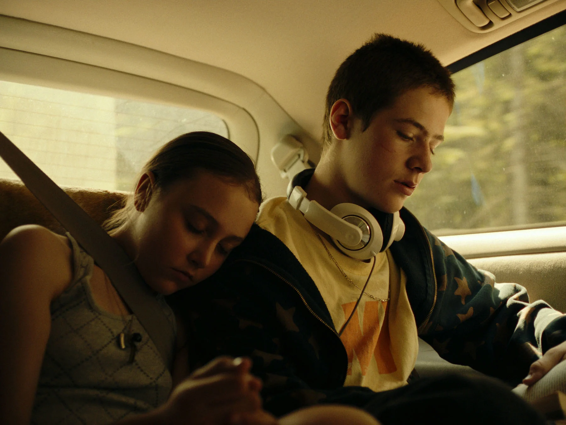 A still from the movie "Invincible" featuring Marc-Antoine and Justine Bernier, played by actors Léokim Beaumier-Lépine and Élia St-Pierre. While Marc reads a book in a car illuminated by a warm light, his younger sister is lying on his shoulder, asleep.
