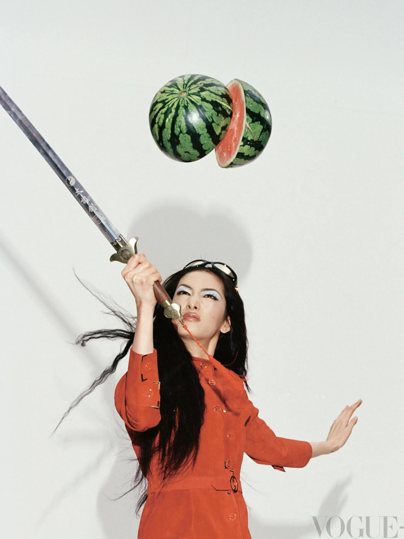 A photograph of model Cici splitting a watermelon in half with an iron sword.
