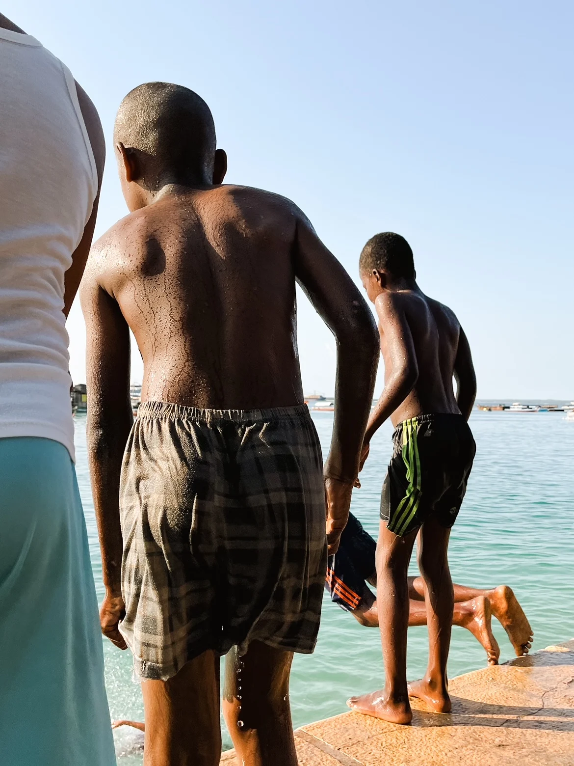 A photograph of some boys playing by the water in Zanzibar, Tanzania. One dives into the water while the others look on. 