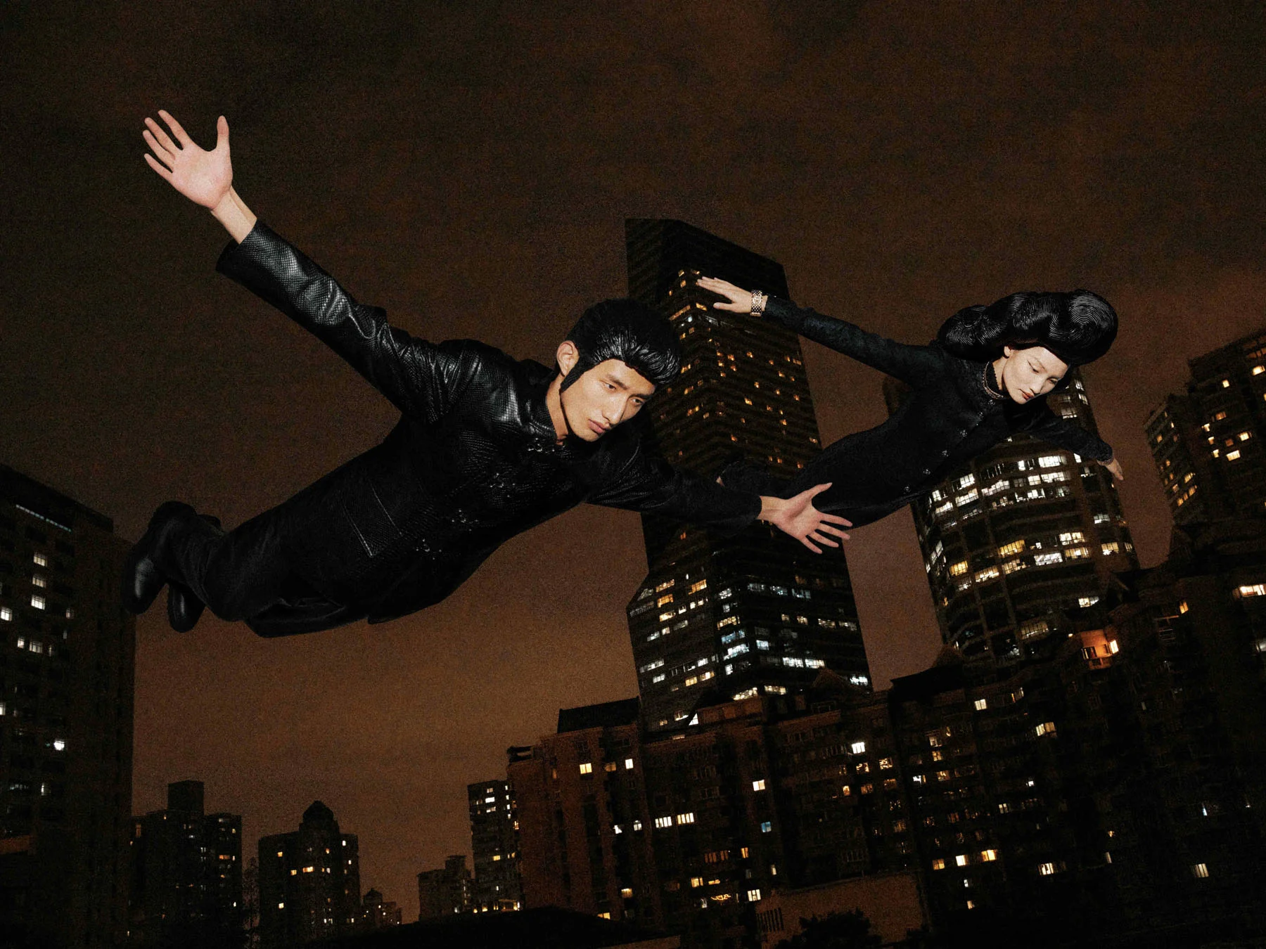 A photograph of male model Huang Liyang and female model Li Qian seemingly flying through the sky surrounded by the skyscrapers of nighttime Shanghai.