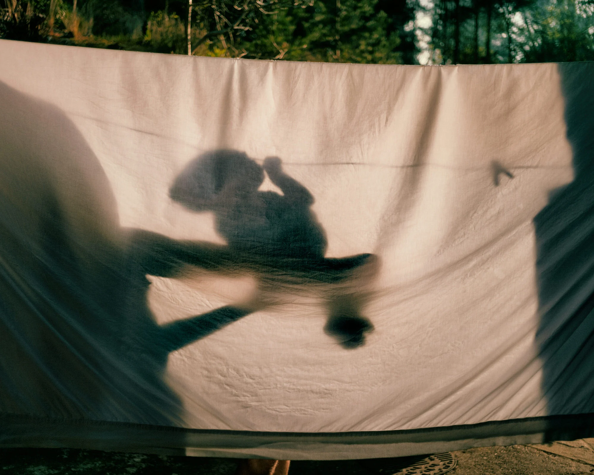 My nephew, Finn, held by his father behind my drying bed sheets late on Saturday afternoon. England, 2020 © Emily Garthwaite