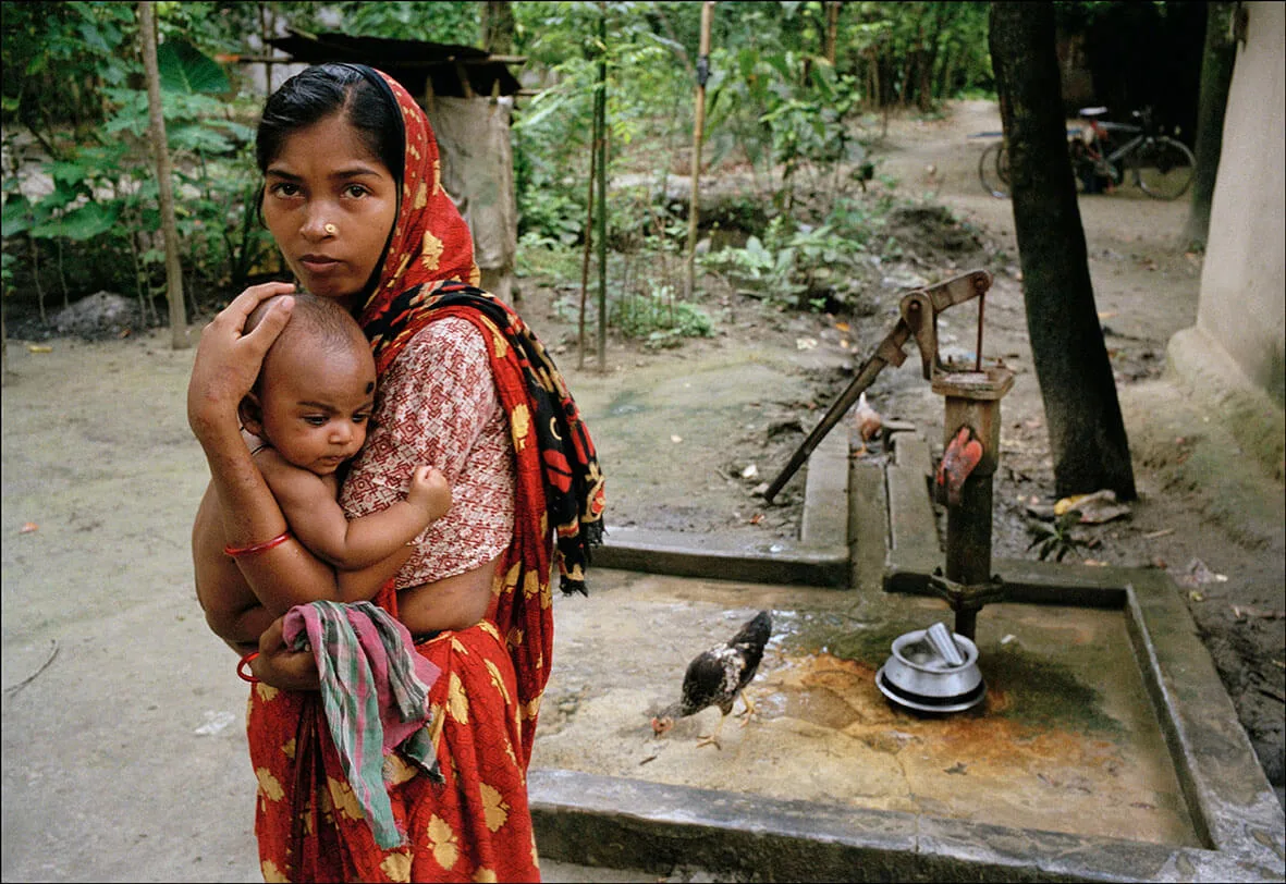 A woman whose arms and sides show the telltale black marks of arsenic poisoning has only this pump for fresh water. It is painted red to indicate the water is contaminated with arsenic. 2000. Bangladesh © Ian Berry/Magnum Photos 