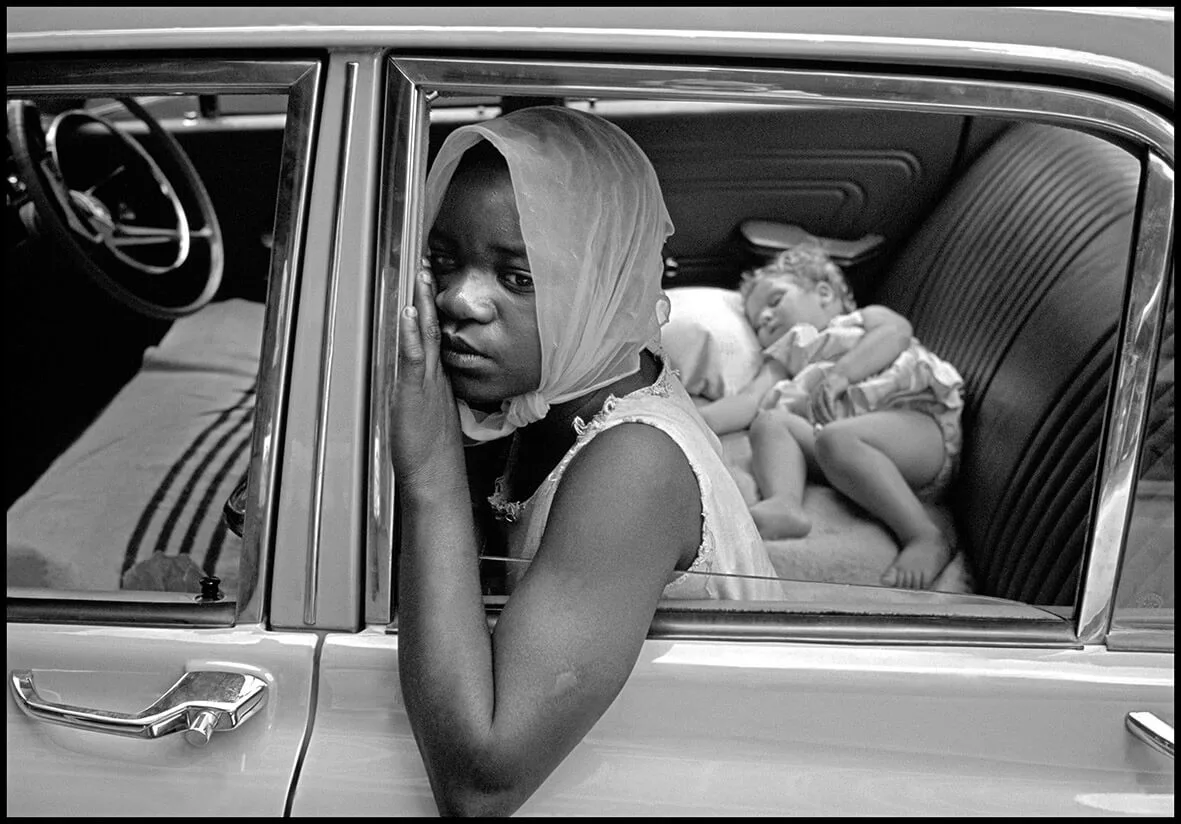 A young black girl, scarcely more than a child herself, looks after a baby girl for a white family. 1969, South Africa. © Ian Berry/Magnum Photos